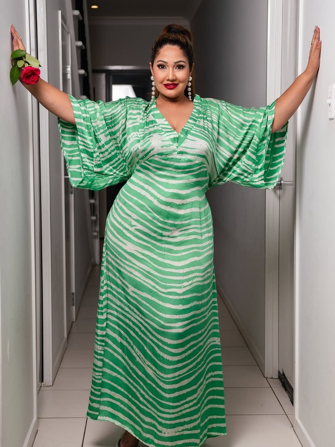 Full-length view of the green batik kaftan, arms outstretched with a red rose in one hand