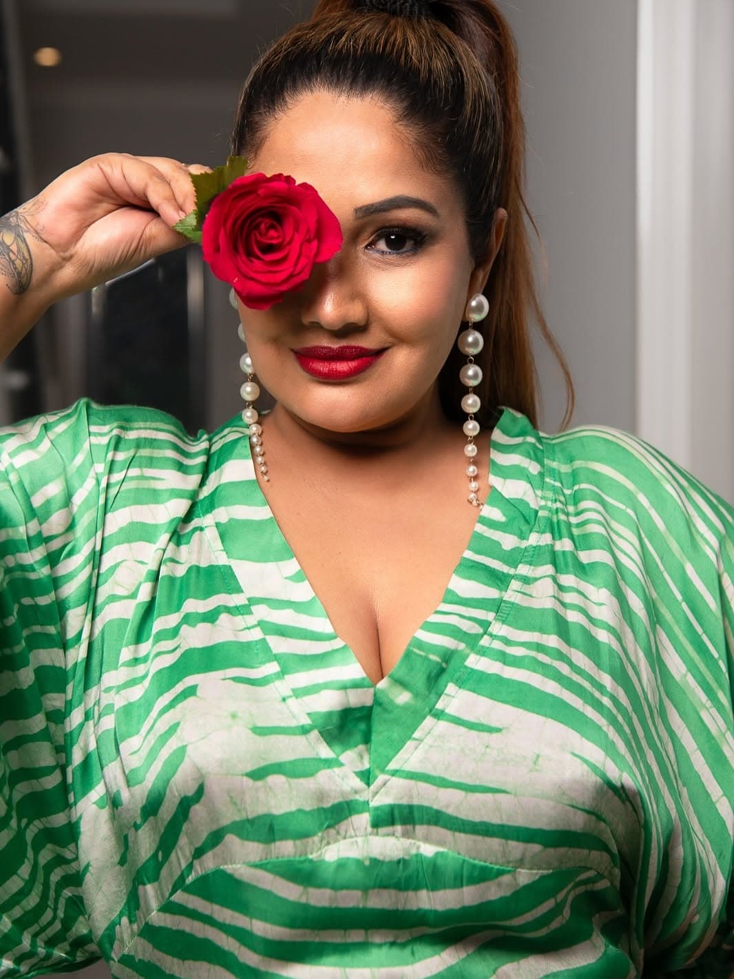 Beauty close-up: a red rose held over one eye, pearl drop earrings and a deep red lip, in a green batik kaftan